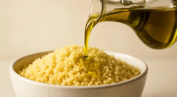 Olio d'oliva versato su couscous in una ciotola, mostrando la differenza tra cous cous e pasta.
