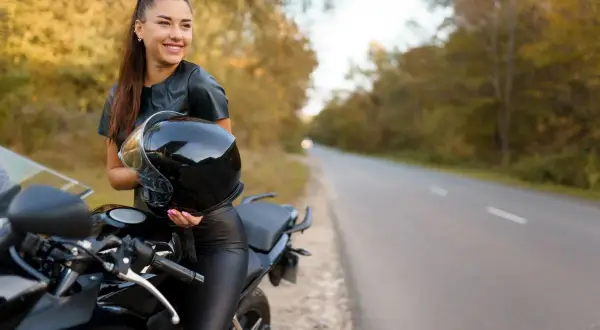 Uśmiechnięta kobieta na motorze, trzymająca kask, gotowa na podróż.