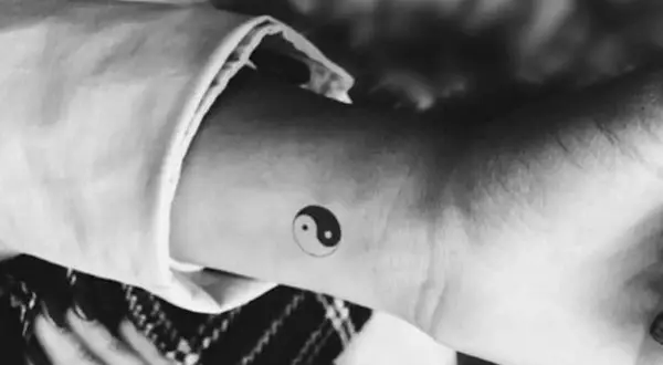 Mały tatuaż yin yang na nadgarstku. Symbolizuje równowagę i harmonię, a jego znaczenie jest głębokie.