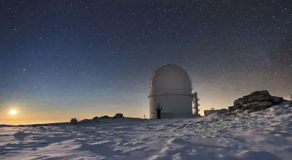 Observatorio en el calar alto bajo un cielo estrellado. La luna ilumina un paisaje nevado y rocoso.