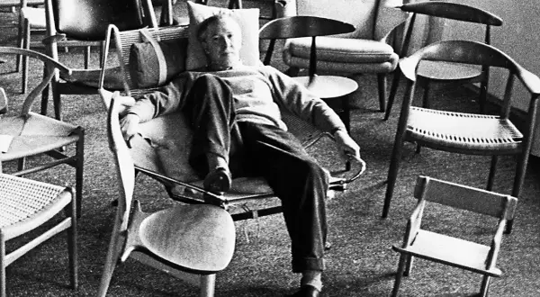 Hans J Wegner, a master of Danish design, relaxes amidst his iconic chairs, surrounded by his timeless creations.