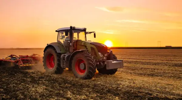 Un tracteur, c'est ce puissant engin vert et rouge qui travaille la terre au coucher du soleil, préparant le champ pour les futures récoltes.