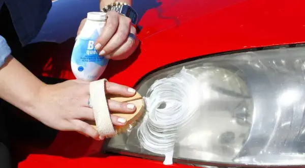 Manos limpiando un faro de coche con pasta blanca para pasar la ITV.