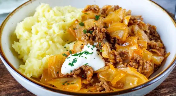 Herzhaftes Gericht mit Kartoffelpüree und geschmortem Kohl mit Hackfleisch als Beilage, garniert mit einem Klecks Sauerrahm und Petersilie.
