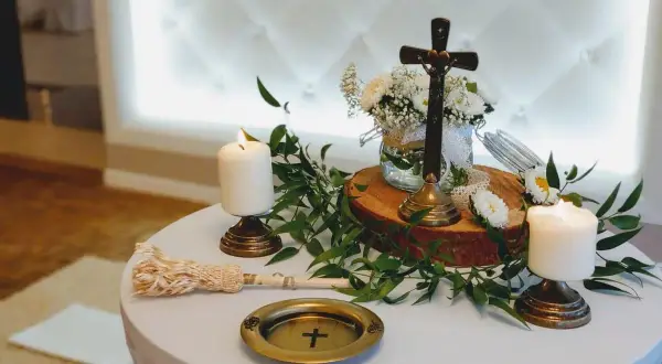 Stół na błogosławieństwo z krzyżem, świecami i bukietem białych kwiatów.