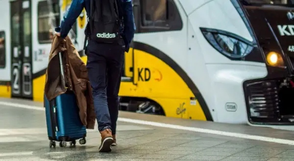 Podróż pociągiem nad morze. Mężczyzna z walizką i kurtką idzie na peronie w stronę nowoczesnego pociągu.