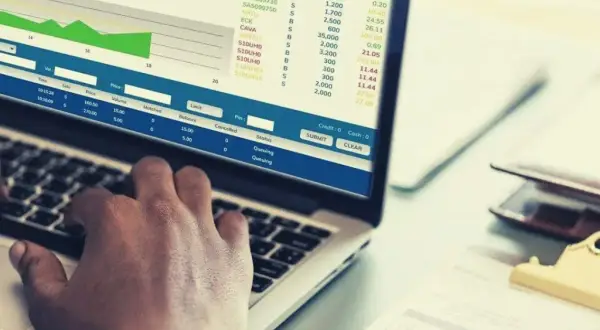 Ręce na klawiaturze laptopa, na ekranie wykresy i tabele z danymi finansowymi, widoczne są też przyciski "SUBMIT" i "CLEAR", sugerujące pracę nad transakcjami, być może w kontekście giełdowym lub analizy danych, np. w eps.