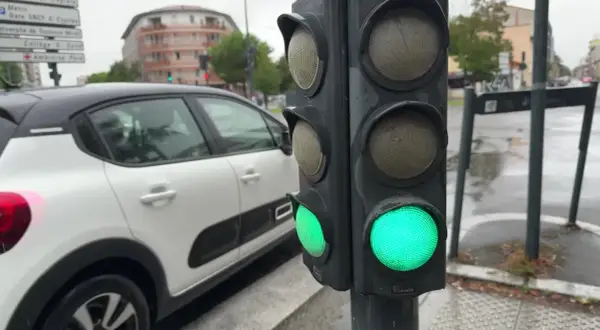 Un feu de circulation vert est allumé, indiquant que la circulation peut passer. Le gyrophare vert signification est la permission de continuer. Une voiture blanche est garée à proximité.