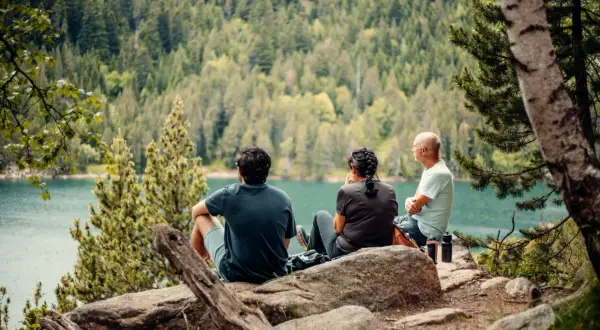 Tres personas disfrutan de las vistas del lago y el bosque, un descanso perfecto en las rutas Vall de Boí.
