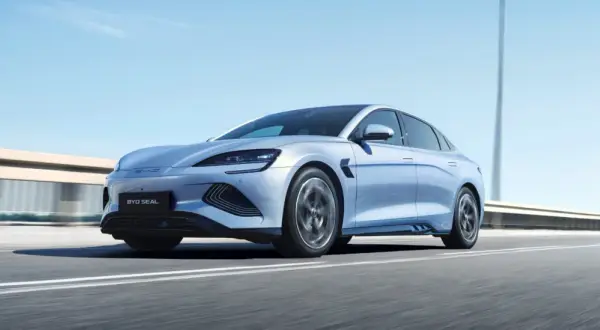 Un elegante veicolo elettrico BYD Seal sfreccia su un'autostrada soleggiata, con il cielo azzurro e le luci stradali sfocate sullo sfondo.