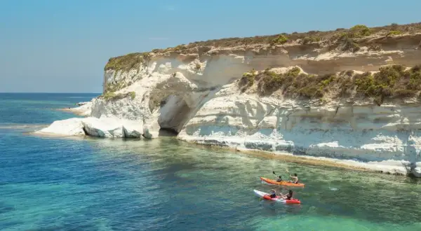 Malta, październik: kajaki w turkusowej wodzie przy klifie z jaskinią. Idealna pogoda na wodne przygody.