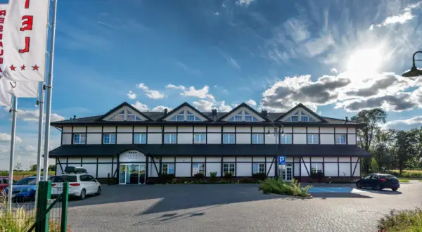 Hotel z białymi ścianami i czarnymi belkami, trzy gwiazdki na fladze, parking.