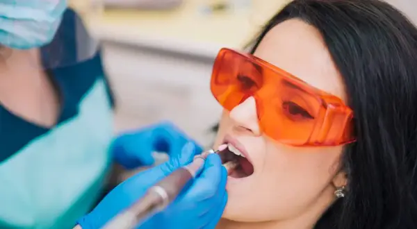 Pacjentka w okularach ochronnych przechodzi zabieg znieczulenia komputerowego zęba. Dentysta w rękawiczkach używa nowoczesnego urządzenia.