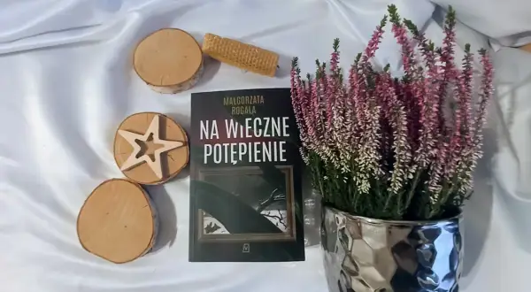 Książka "Na wieczne potępienie" Małgorzaty Rogali, wrzosy w ozdobnej doniczce, drewniane krążki i wafel.