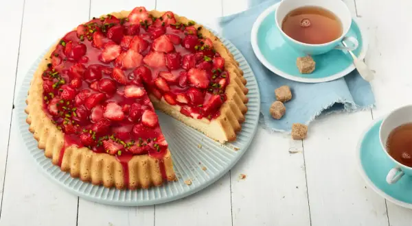 Ein schneller Erdbeerkuchen mit Paradiescreme, belegt mit frischen Erdbeeren und Pistazien. Dazu eine Tasse Tee.