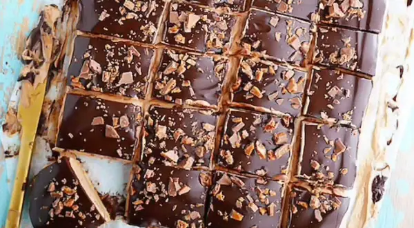 Biskvier i långpanna från Lindas bakskola, täckta med choklad och strössel. En gyllene kniv ligger bredvid.
