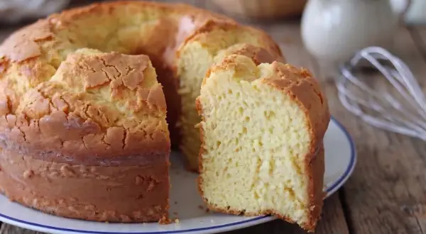Il ciambellone della nonna, soffice e dorato, pronto per essere gustato. Sullo sfondo, uova e latte, ingredienti essenziali.
