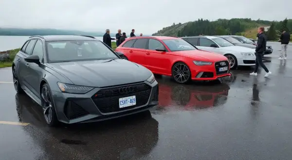 Szare i czerwone Audi RS6 C8 stoją obok siebie na mokrym parkingu.
