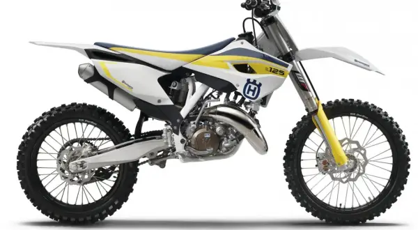Motocykl Husqvarna cross 125 w białej, żółtej i niebieskiej kolorystyce, gotowy do jazdy po torze.