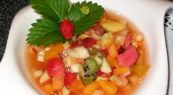 Salade de fruits maison colorée, garnie d'une fraise et de feuilles de fraisier.