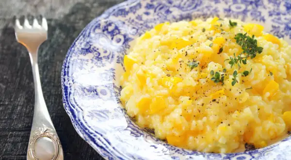 Pyszny, kremowy ryż do risotto z kawałkami dyni, posypany świeżym tymiankiem i pieprzem. Obok leży elegancki widelec.