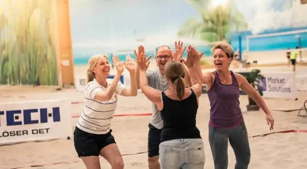 Fyra glada kollegor ger varandra high-fives på en sandstrand. Perfekta tips på aktiviteter med kollegor för teambuilding!
