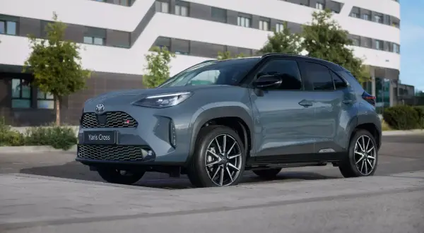Szary Toyota Yaris Cross GR Sport zaparkowany przed nowoczesnym budynkiem. Zastanawiasz się, ile kosztuje Toyota Yaris?
