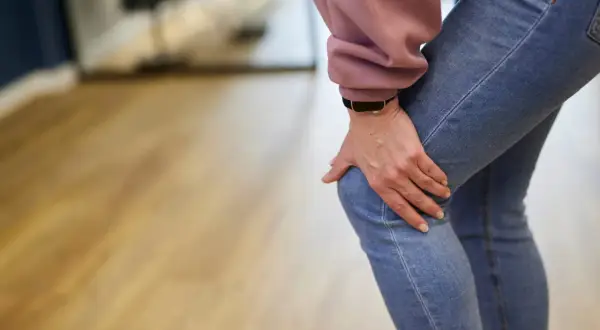 Frau hält schmerzhaft ihr Knie, was auf einen Meniskusriss hindeutet. Mögliche meniskusriss behandlung wird gesucht.