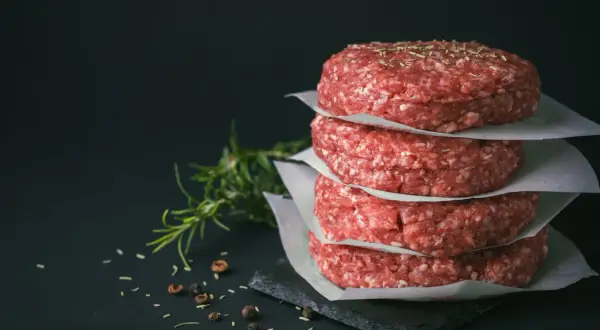Stos surowych kotletów na burgery, idealne mięso na burgery, z gałązką rozmarynu i pieprzem w tle.