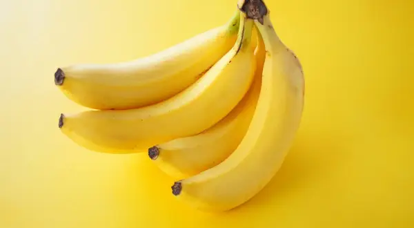 Pęczek żółtych bananów na żółtym tle. Zastanawiasz się, ile kcal ma banan?
