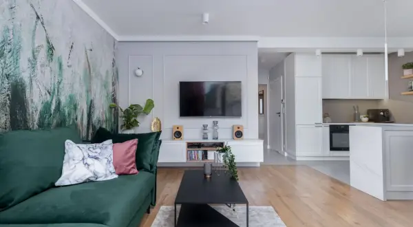 Nowoczesny pokój z telewizorem, zieloną kanapą i designerską tapetą. W tle widać kuchnię.