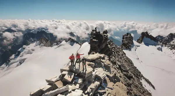 Des alpinistes atteignent le sommet rocheux, dominant un océan de nuages. Un panorama à couper le souffle, un véritable grand paradis.
