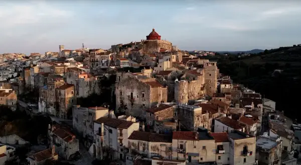 Antico borgo di Vico del Gargano, con case in pietra e tetti rossi che si aggrappano alla collina, dominato da una chiesa con cupola rossa.