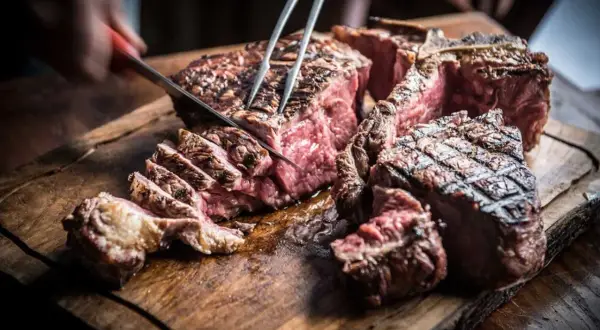 Una succulenta fiorentina steak, tagliata al sangue su un tagliere di legno rustico, con un coltello che affonda nella carne.