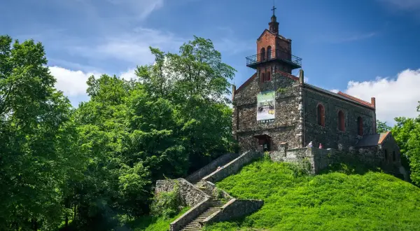 Kamienny kościół na wzgórzu, z kamiennymi schodami prowadzącymi do wejścia. Wokół bujna zieleń, idealne miejsce na odkrywanie dzierżoniów atrakcje.