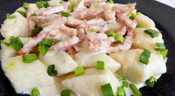 Pyszne kopytka z sosem śmietanowym i kawałkami wędzonego boczku, posypane szczypiorkiem.