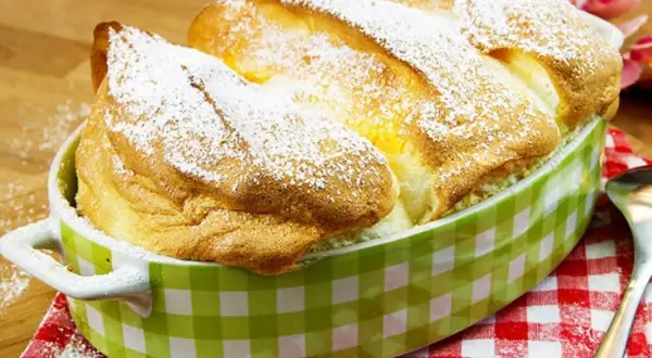 Ein goldbrauner, luftiger Salzburger Nockerl-Auflauf, bestäubt mit Puderzucker, in einer grünen Karamikform.