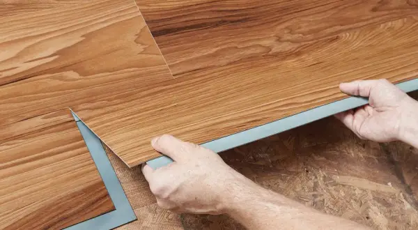 Hands installing wood-look vinyl plank flooring. Once installed, you can walk on vinyl plank flooring immediately.