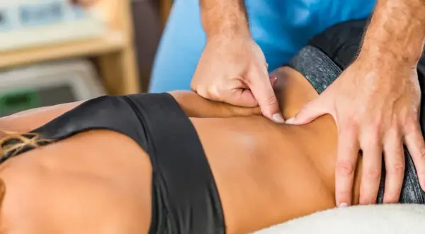 Mains d'un kinésithérapeute travaillant sur un dos contracté, soulageant la tension musculaire.