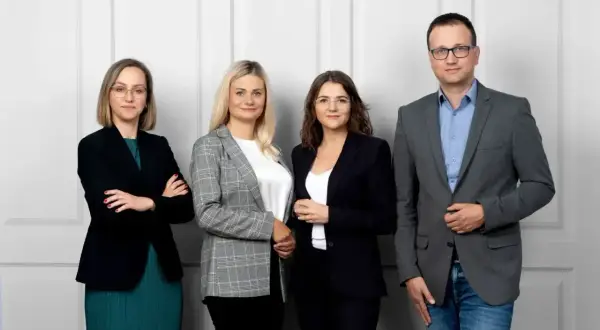 Cztery osoby w strojach biznesowych stoją obok siebie na jasnym tle.