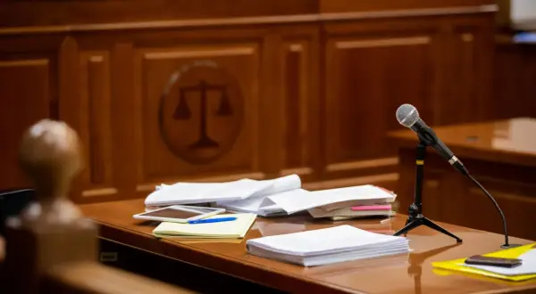 Stół w sali sądowej z dokumentami, mikrofonem i symbolem sprawiedliwości w tle. Czas na rozprawę sądową.