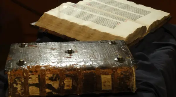 Stary, zniszczony księgozbiór w stylu biblijnym, z metalowymi okuciami i otwartą księgą pełną tekstu.
