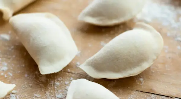Surowe, niegotowe pierogi na drewnianej desce. To ciasto na pierogi bez jajka, gotowe do nadziewania.