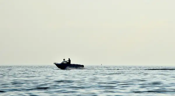 Due persone su un'imbarcazione con potenti motori marini navigano su un mare calmo, lasciando una scia d'acqua.