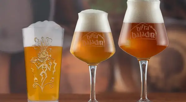 Tre bicchieri di birra, uno tipo pinta americana, con schiuma abbondante e logo Baladin inciso.