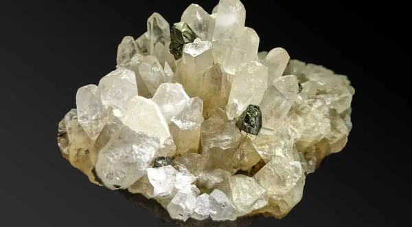 Ein Cluster aus klaren, facettierten Quarz-Kristallen mit dunklen Einschlüssen. Was ist Quarz? Ein faszinierendes Mineral!