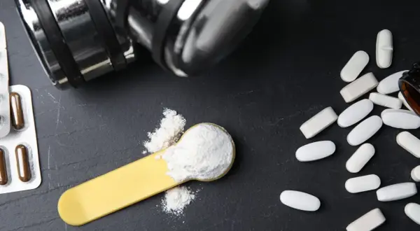 Bilancia, pillole e polvere bianca su un cucchiaio: cosa è meglio, proteine o aminoacidi per aumentare massa?