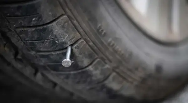 Un clou rouillé est planté dans la bande de roulement d'un pneu usé, prêt à causer une crevaison.