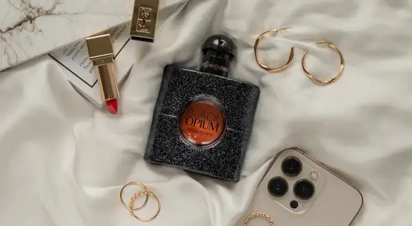Elegancka kompozycja z flakonem perfum **black opium**, złotą szminką, pierścionkami i telefonem.