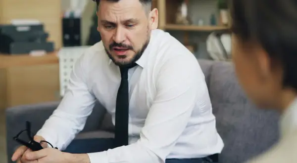 Mężczyzna w białej koszuli i krawacie, trzymający okulary, zastanawia się, jak inteligentnie zakończyć rozmowę.